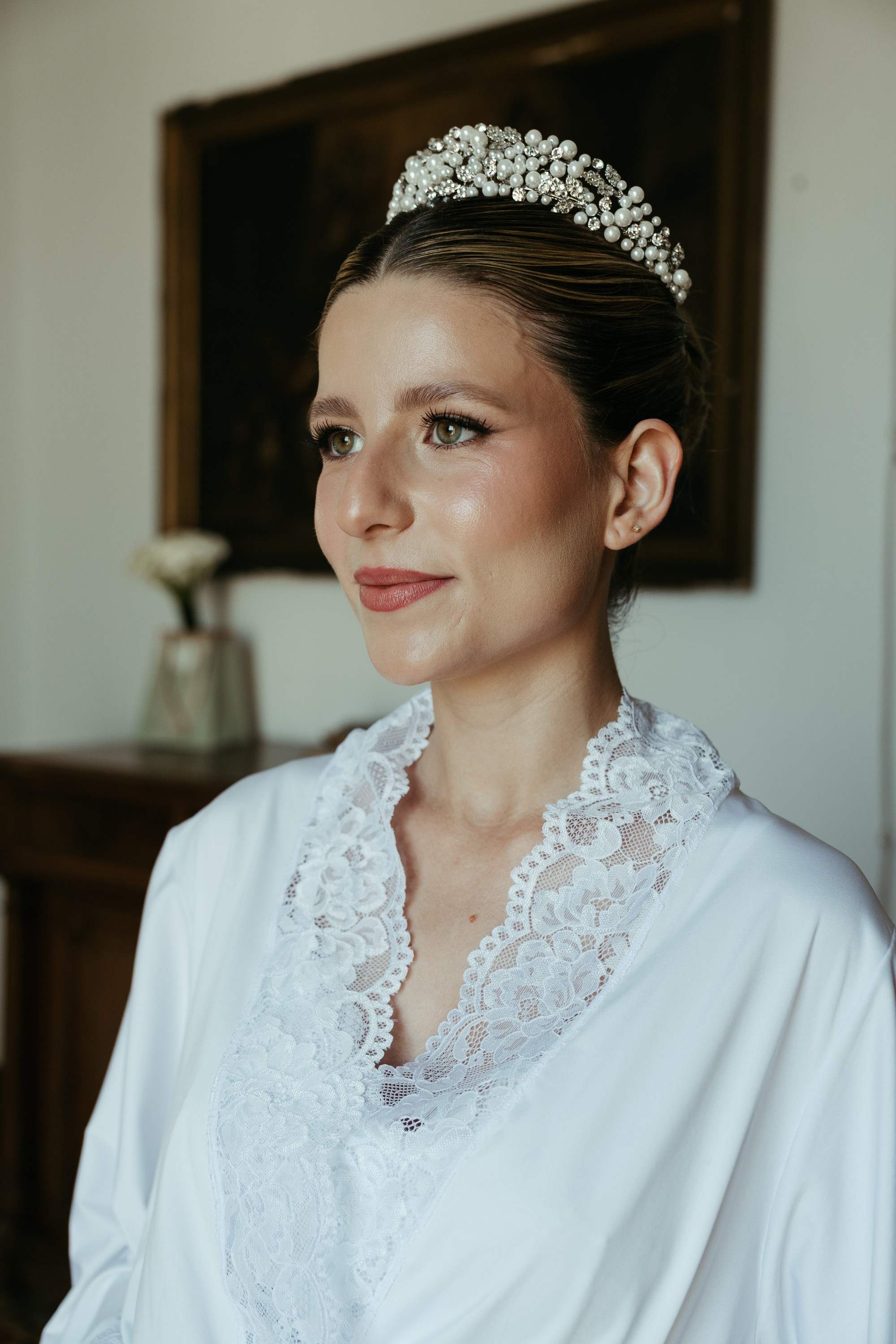 Retrato de la novia con tiara y bata de encaje junto a la ventana