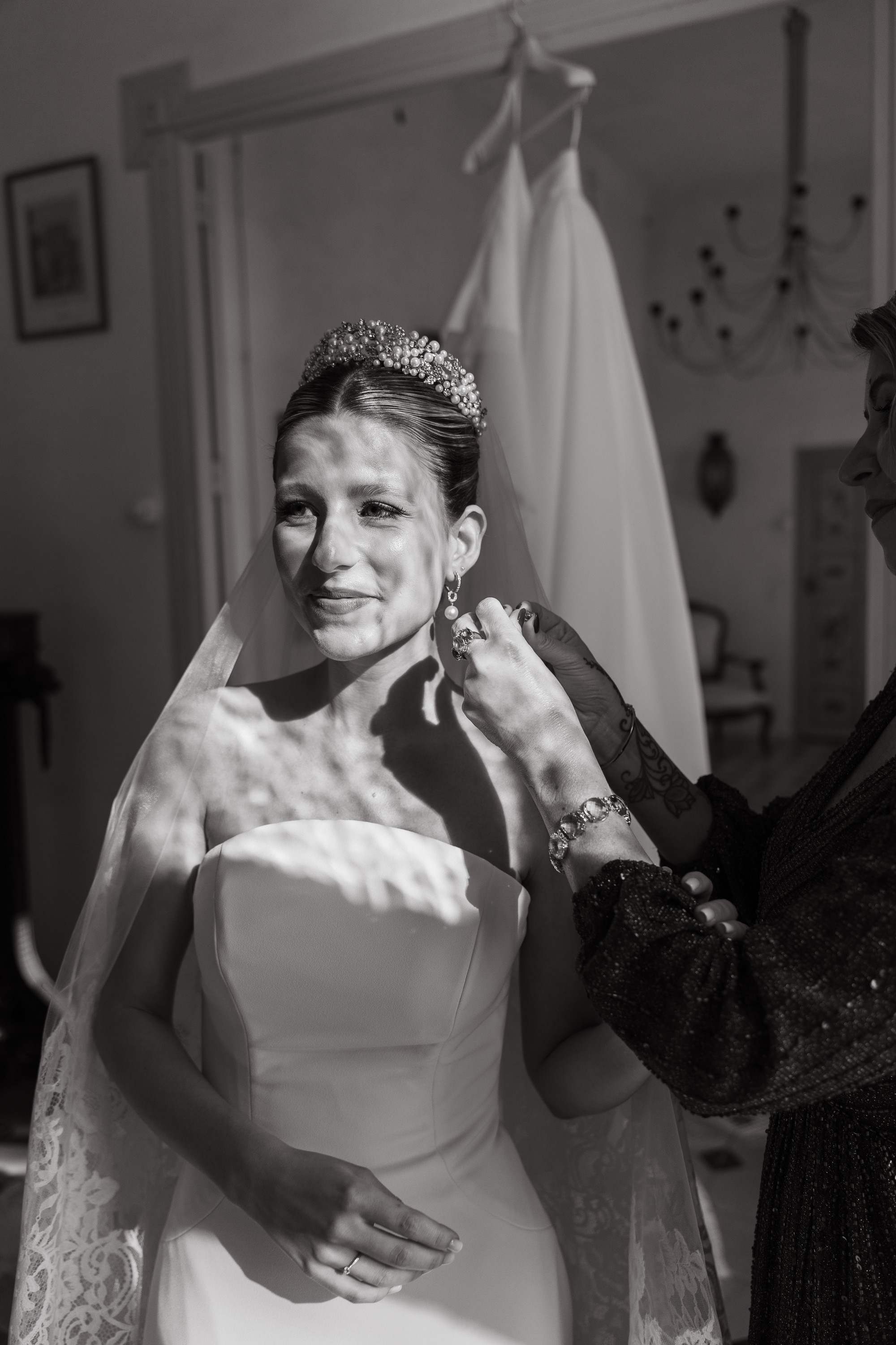 La novia se emociona bajo el velo mientras la ayudan a prepararse, en blanco y negro